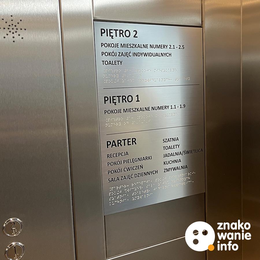 Informacyjna tablica z laminatu w windzie z alfabetem Braille’a Informacyjna tablica z laminatu w windzie z alfabetem Braille'a